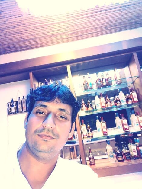 Close-up shot of Ryan Reynolds standing next to an Aviation Gin display in a liquor store. He is smiling and holding a bottle of the gin, and the display is well-stocked with prominent branding.