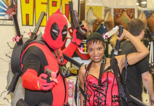 A professional cosplayer posing for a photoshoot at a comic con, dressed as a popular superhero character. The cosplayer is surrounded by fans, showcasing their popularity and influence.
