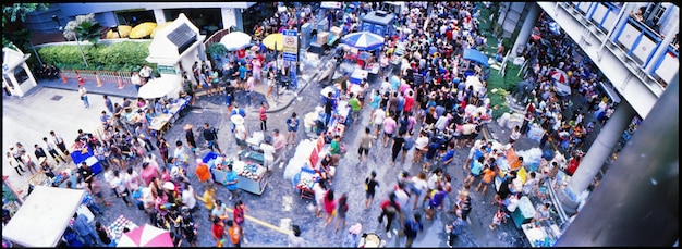 A panoramic view of the San Diego Comic-Con, showing a massive crowd of attendees, elaborate booth displays, and cosplayers posing for photos. The atmosphere is energetic and vibrant.