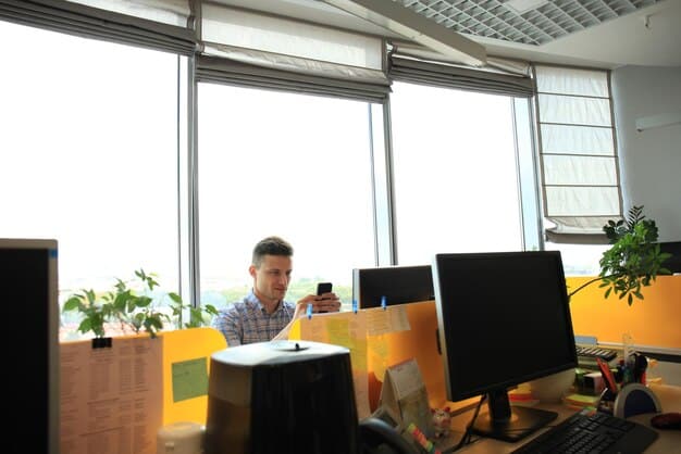A brightly lit office space with multiple monitors displaying lines of code. Several young adult developers are engaged in intense discussions, pointing to screens, and gesturing with their hands. The atmosphere reflects collaboration and problem-solving within a game development team.